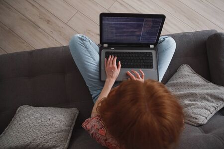 Young woman programmer working on laptop from home, freelance, social distancing and remote work. View from aboveの写真素材