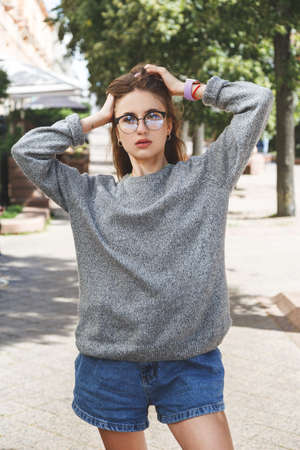 Young woman in gray sweater and denim shorts in the street.の写真素材
