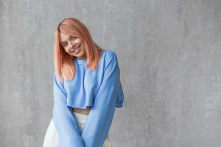 Portrait of young embarrassed woman wearing ripped pants sportswear standing at concrete wallの写真素材