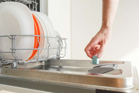 Man puts a chemical dishwasher tablet into the dishwasher machineの写真素材