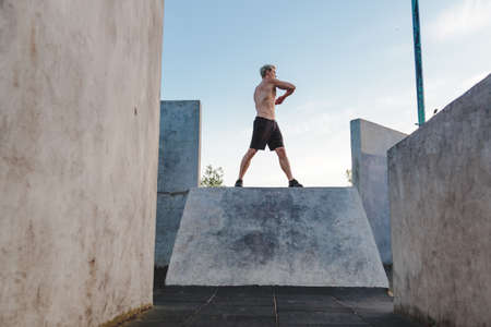 Fitness man warming up outdoors on sports ground and listen to music in headphones. Rotates body and swings handsの写真素材