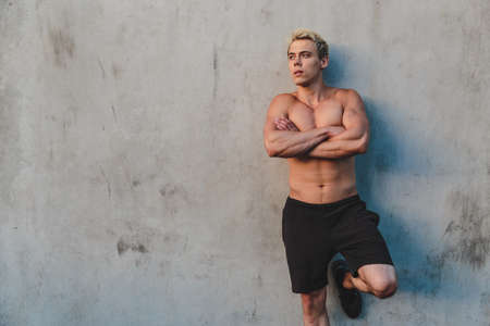 Natural portrait of young athletic shirtless man standing near concrete wall.の写真素材