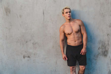 Natural portrait of young athletic shirtless man standing near concrete wall.の写真素材