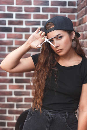 Young caucasian barber woman holding a straight razor and scissors against brick wallの写真素材