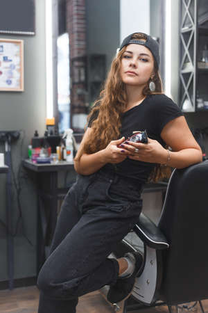 Young caucasian barber woman holding a straight razor and scissors standing at workplaceの写真素材