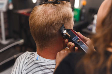 Female barber in mask cuts a man hairs with hair clipper. hairstyle during social distancingの写真素材