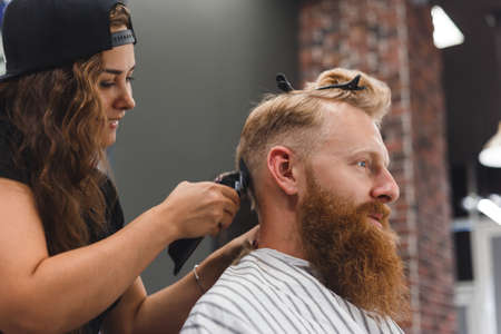 Female barber in mask cuts a man hairs with hair clipper. hairstyle during social distancingの写真素材