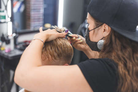 Woman barber cutting hair to a bearded man in face mask. Quarantine haircut concept.