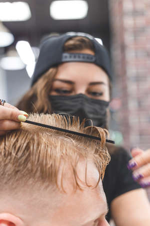 Woman barber cutting hair to a bearded man in face mask. Quarantine haircut concept.の写真素材