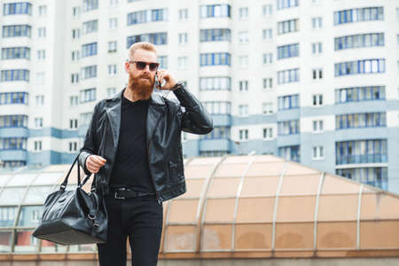 Caucasian man walks around the city with leather bag and talking on the phone.の写真素材