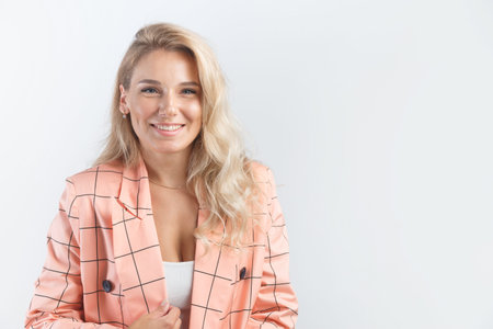 Blonde smiling woman with curly hairstyle dressed in a formal pink jacket on white background.