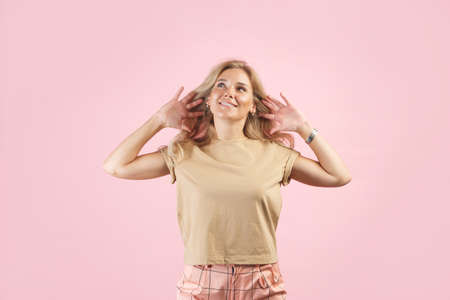 Gossip or rumors concept. Colorful portrait of amazed young woman with palms near her ears. Pink backgroundの写真素材