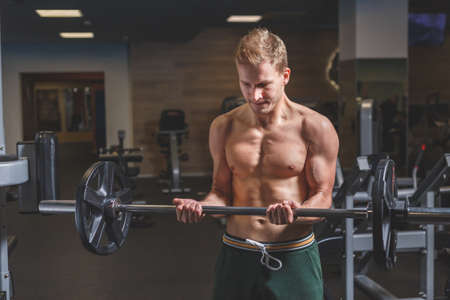 Muscular man working out in gym doing exercises with barbell at biceps, beginner maleの写真素材