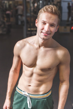 Sexy portrait of a young muscular male model with great happy smile in the gym