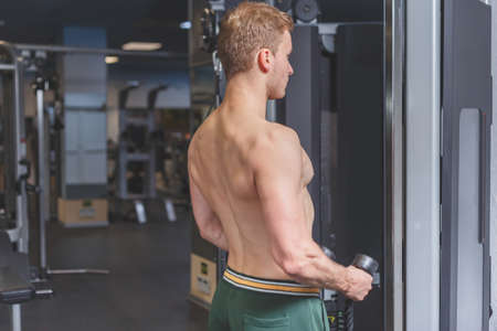 Strong shirtless male athlete concentrated on an excersise on a hand pull machine, pumping up his triceps in a dark gym surrounded by smokeの写真素材