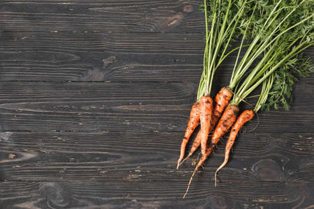 Bunch of ripe carrots on a black wooden background with space for textの写真素材