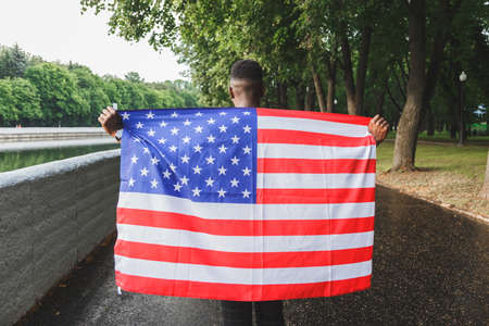 Black african-american man holding USA flag from his back walking outdoorsの写真素材