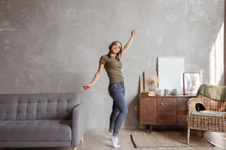Young woman with wireless headphones dancing and listening to music at homeの写真素材