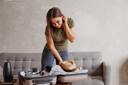 Suitcase preparation for a vacation trip after lock down. Young woman checking clothes and stuff in luggage on the sofa at home before travelの写真素材
