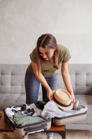 Suitcase preparation for a vacation trip after lock down. Young woman checking clothes and stuff in luggage on the sofa at home before travelの写真素材