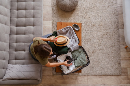 Suitcase preparation for a vacation trip. Young woman checking clothes and stuff in luggage on the sofa. View from aboveの写真素材