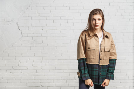 Young beautiful woman in autumn jacket stands near white brick wall. Portrait with copy spaceの写真素材