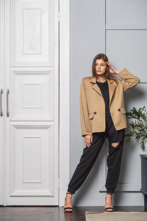 Young brunette woman with long hair wearing a stylish fashionable jacket and black pants. Standing in interior near doorの写真素材