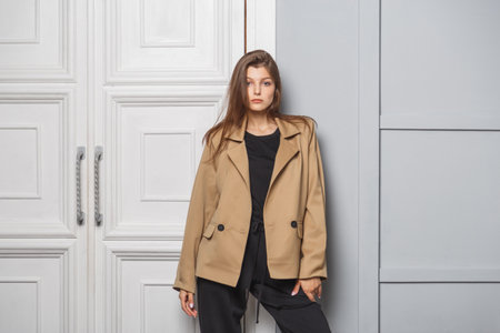Young brunette woman with long hair wearing a stylish fashionable jacket and black pants. Standing in interior near doorの写真素材