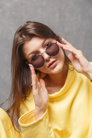 Young woman in yellow sweatshirt and sunglasses on a gray backgroundの写真素材