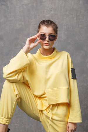 Young woman in yellow sweatshirt and sunglasses on a gray backgroundの写真素材