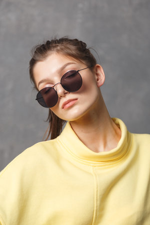 Young woman in yellow sweatshirt and sunglasses on a gray backgroundの写真素材
