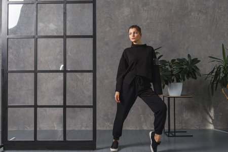 Young woman in black sportswear, pants and sweatshirt. Concept of fashionable sport outfit, indoors photo. Copy space.の写真素材