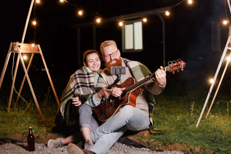 Young couple on a picnic with a guitar take a selfie or video communication with friends or relativesの写真素材