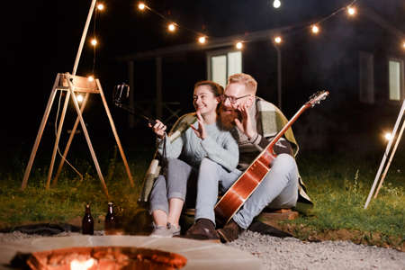 Happy caucasian couple, brunette woman and bearded man with guitar at picnic in countryside. Funny couple making selfie, smiling and have fun together.の写真素材