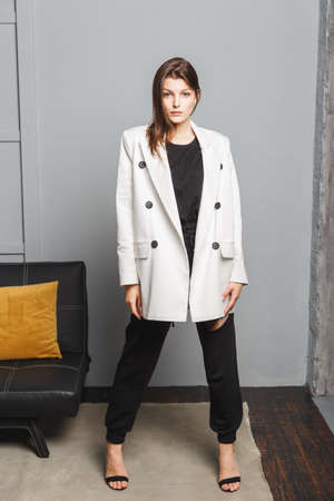 Young elegant woman in white oversize blazer and black ripped pants. Interior portraitの写真素材