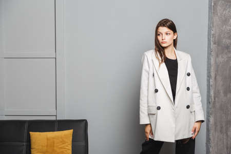 Young elegant woman in white oversize blazer and black ripped pants. Interior portraitの写真素材