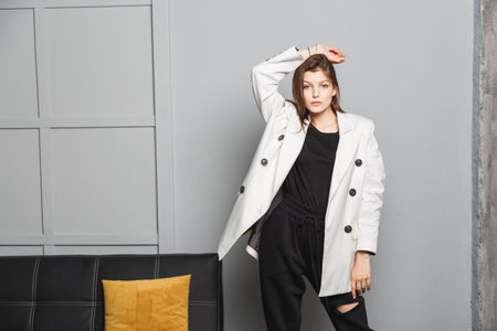 Young elegant woman in white oversize blazer and black ripped pants. Interior portraitの写真素材