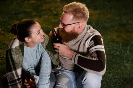 Friends having fun on the night picnic with drinks. Young caucasian couple at bbq in countrysideの写真素材