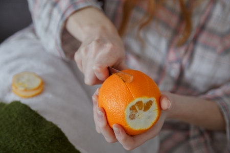 Close up view on women hand peeling an orange by segments with knifeの写真素材