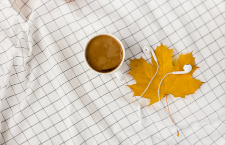 Autumn composition. Cup of coffeecup, autumn leaves and earphones on white checkered cloth. Flat lay, top view, copy spaceの写真素材