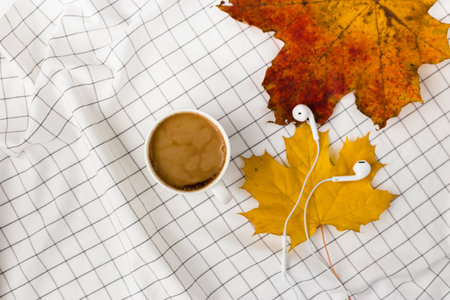 Autumn composition. Cup of coffeecup, autumn leaves and earphones on white checkered cloth. Flat lay, top view, copy spaceの写真素材