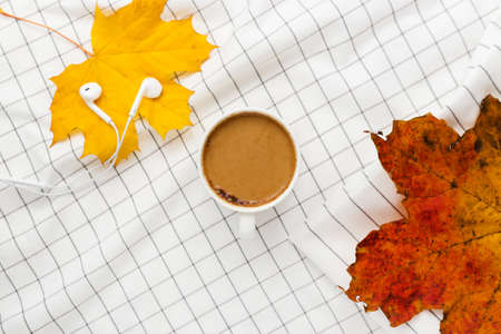 Autumn composition. Cup of coffeecup, autumn leaves and earphones on white checkered cloth. Flat lay, top view, copy spaceの写真素材