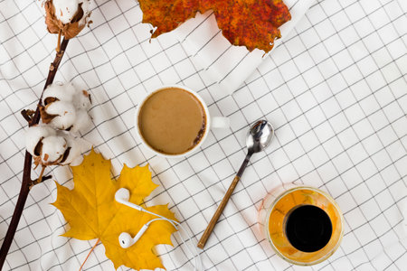 Autumn composition. Cup of coffeecup, autumn leaves and earphones on white checkered cloth. Flat lay, top view, copy spaceの写真素材