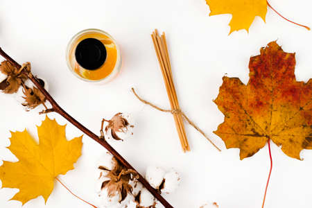 Autumn vibe composition. Blank greeting card mockup. PErfume jar, colorful maple leaves. White table background. Flat lay, top view.の写真素材