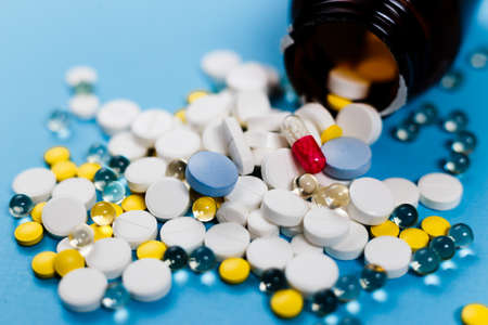 Medical bottle and medication pills spilling out on to pastel blue background. Healthcare, pharmacy, medicine conceptの写真素材