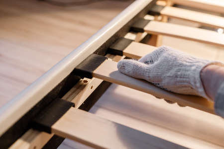 Male workers hand in glove assembling bed, connecting slats to bed frameの写真素材
