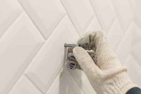 Workers hand in glove inserts wall pvc dowel in wall cladded with tile ceramicの写真素材