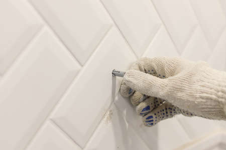 Workers hand in glove inserts wall pvc dowel in wall cladded with tile ceramicの写真素材