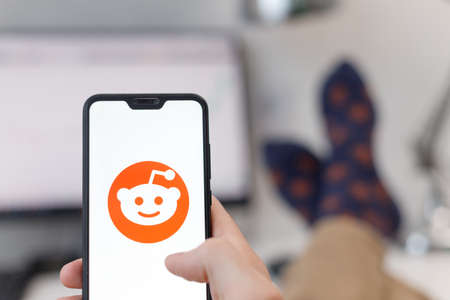 Minsk, Belarus - 31, January, 2021: Reddit logo on smartphone screen in male hands with his feet on tableのeditorial素材