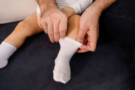 Young father is putting socks on his baby son, sitting on sofaの写真素材